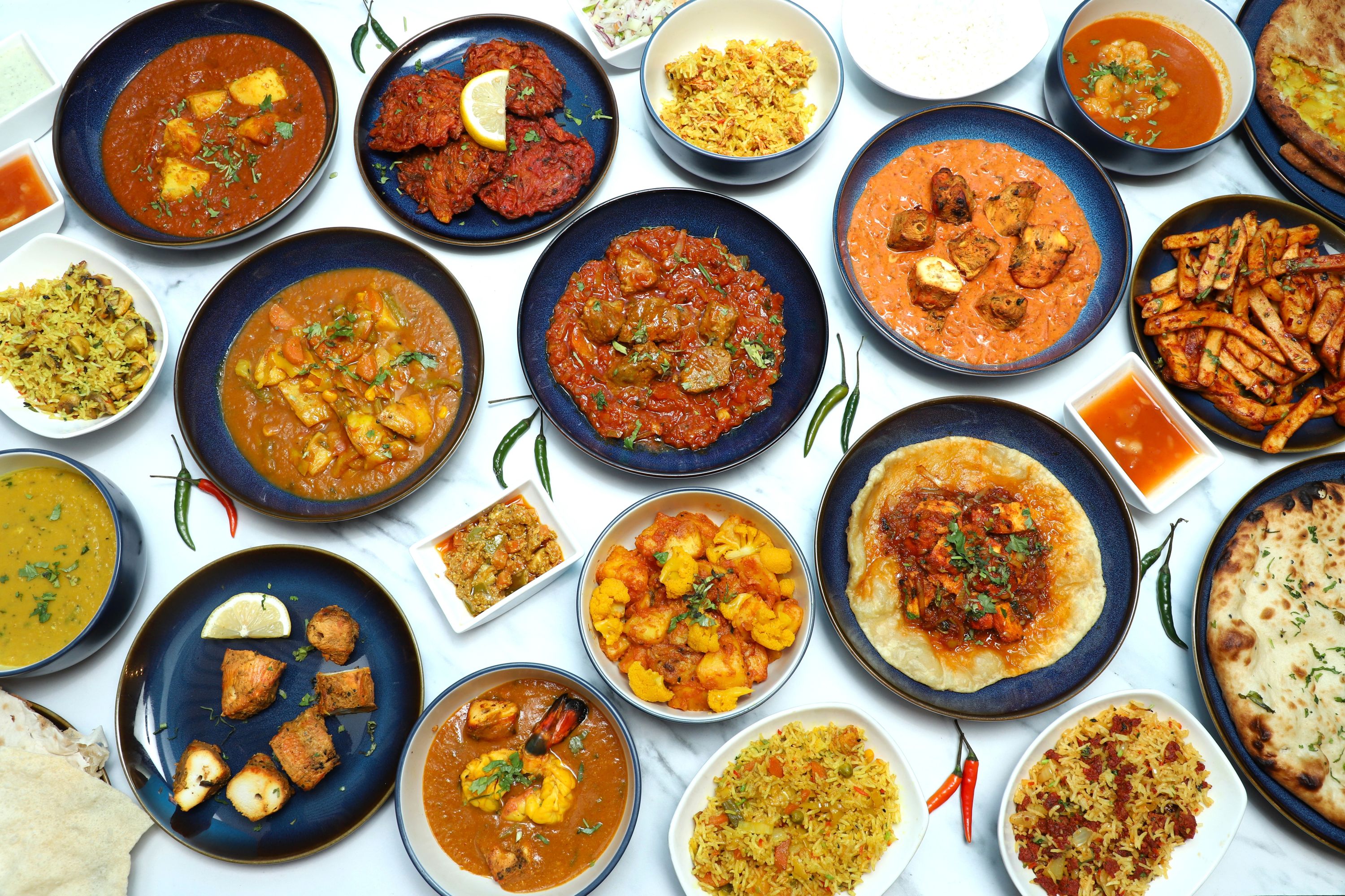 An overhead shot of various colourful Indian dishes in blue and white bowls, with rice, curry, naan, and chutneys.
