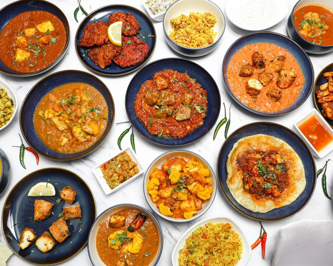 An overhead shot of various Indian curries, rice, appetizers, and breads arranged on a white table.