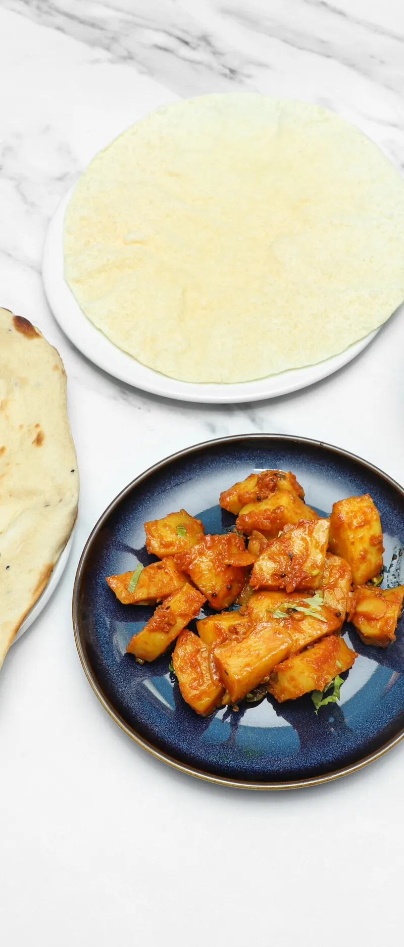 Indian naan bread, white rice, chicken curry, and aloo gobi on white marble surface
