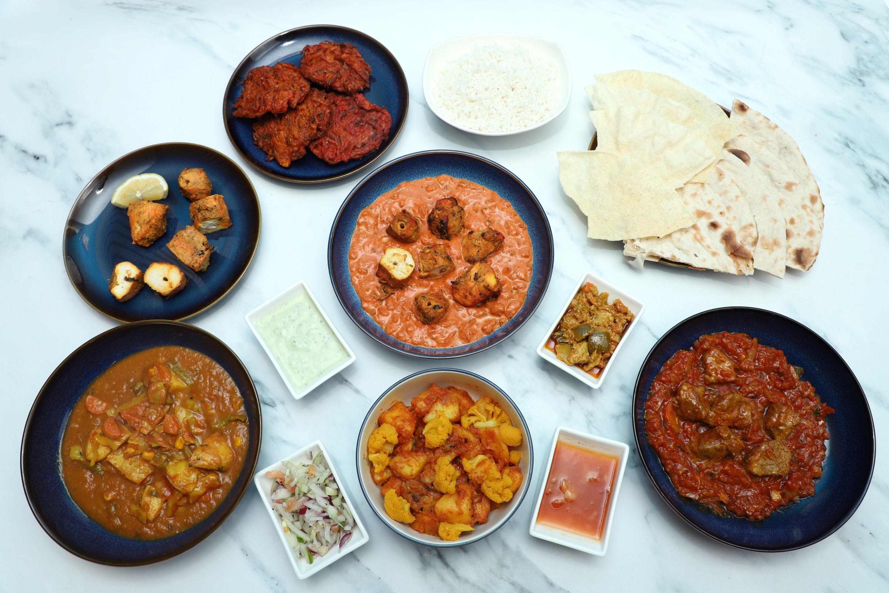 Table of Indian dishes: samosas, tandoori paneer, curries, rice, naan, poppadoms, and chutneys.