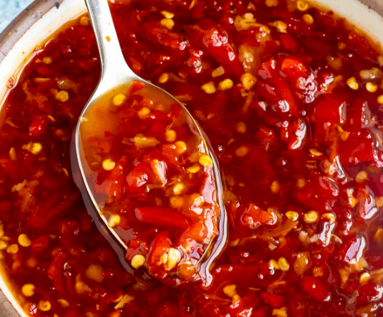 A close-up of sweet chilli dip in a bowl being scooped by a spoon