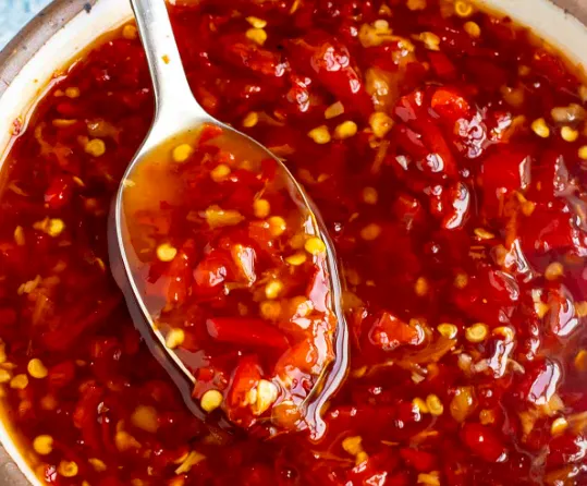 A close-up of sweet chilli dip in a bowl being scooped by a spoon