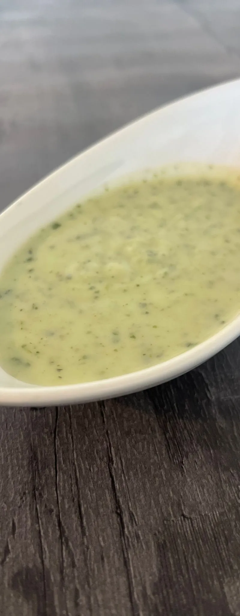 Light green mint sauce with visible herb flecks in an elegant white, boat-shaped dish on a dark wooden surface.