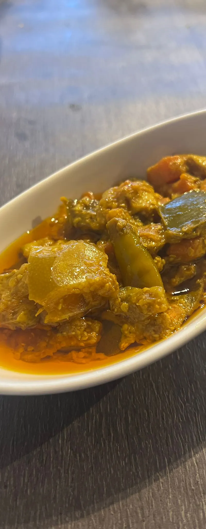 Indian pickle with green, orange, and yellow pieces in a white boat-shaped dish on a dark wooden table.