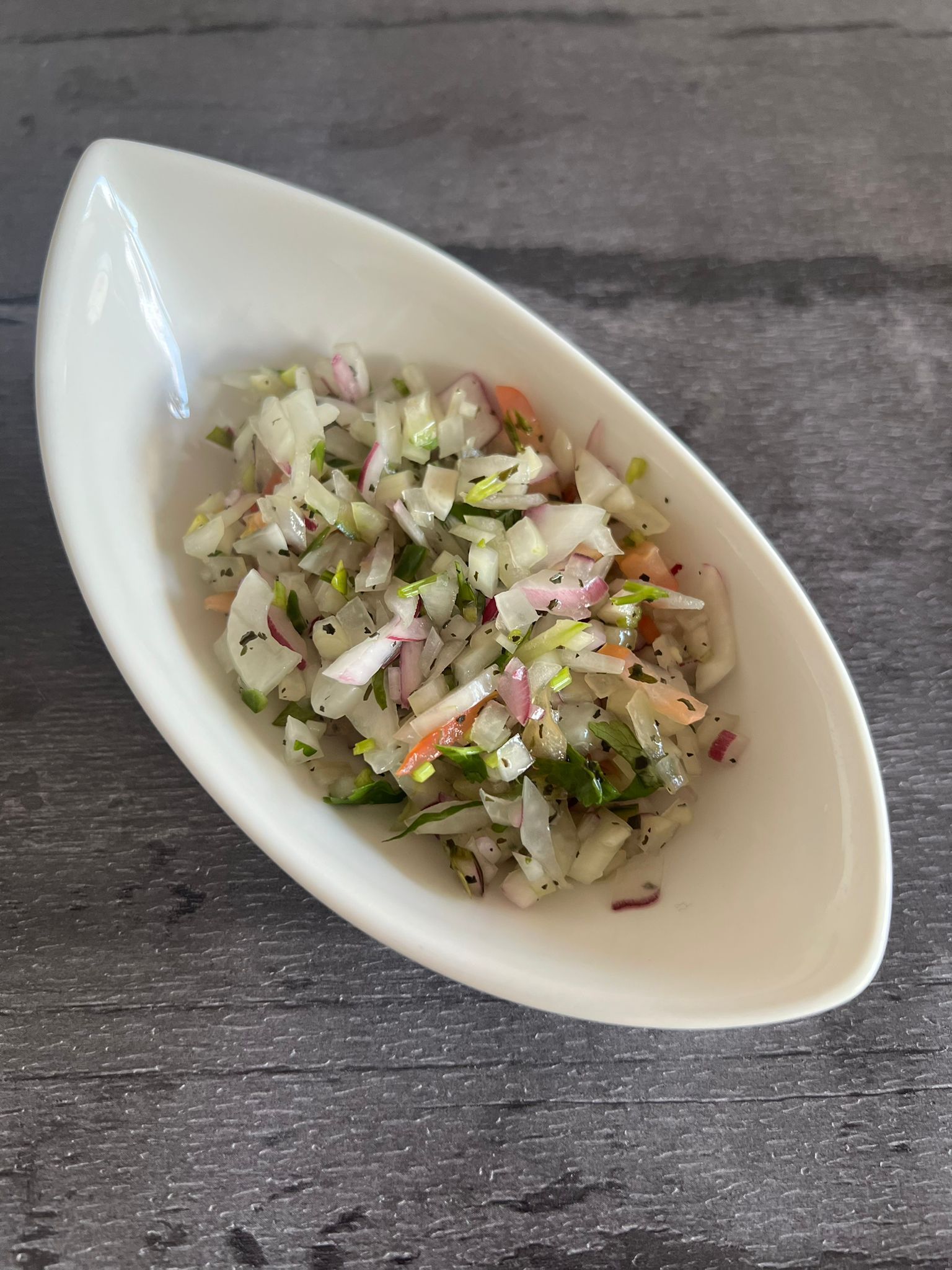 Close-up of a white boat-shaped bowl filled with finely diced onion, red onion, and herbs
