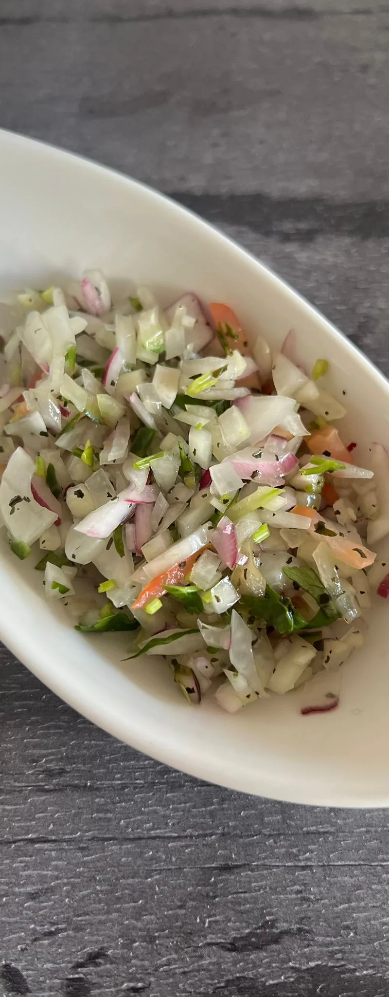 Close-up of a white boat-shaped bowl filled with finely diced onion, red onion, and herbs