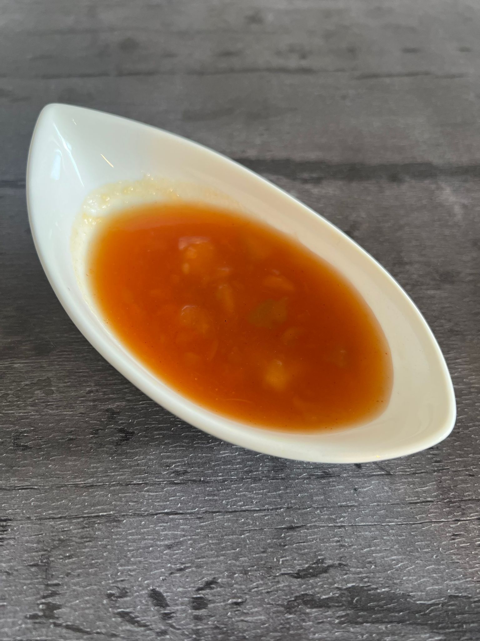 Orange sweet chili sauce with visible herbs and spices in an elongated white ceramic dish