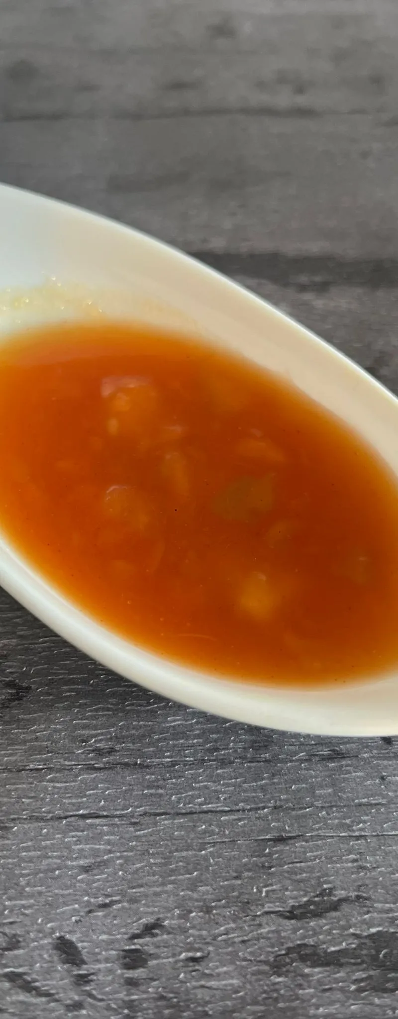 Orange sweet chili sauce with visible herbs and spices in an elongated white ceramic dish