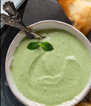 Close-up of a white bowl filled with green mint and coriander chutney, garnished with fresh mint leaves