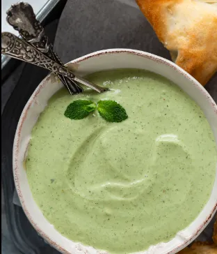 Close-up of a white bowl filled with green mint and coriander chutney, garnished with fresh mint leaves