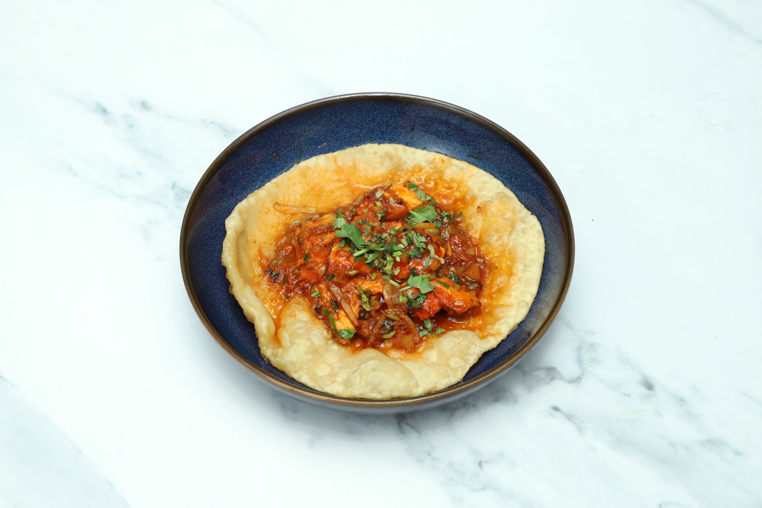 Chilli Paneer Puri, a savoury deep-fried Indian bread with chilli paneer curry, in a dark blue bowl.