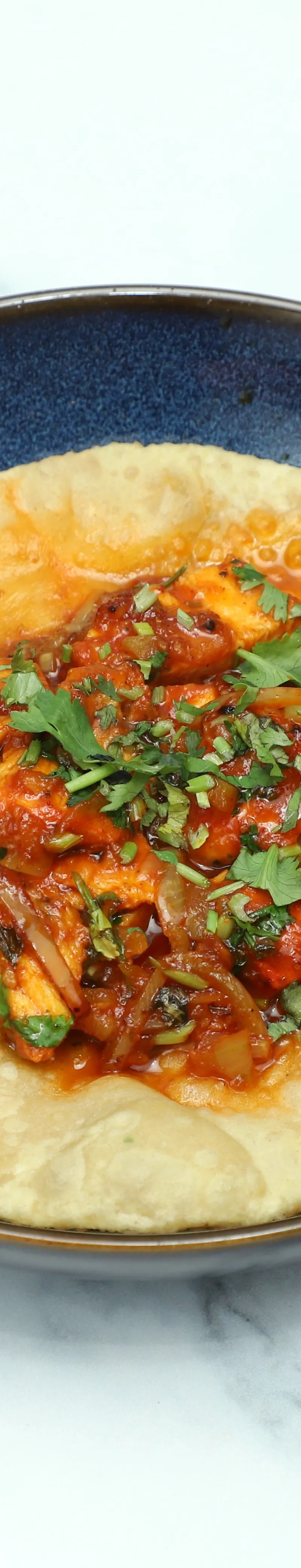 Chilli Paneer Puri, a savoury deep-fried Indian bread with chilli paneer curry, in a dark blue bowl.