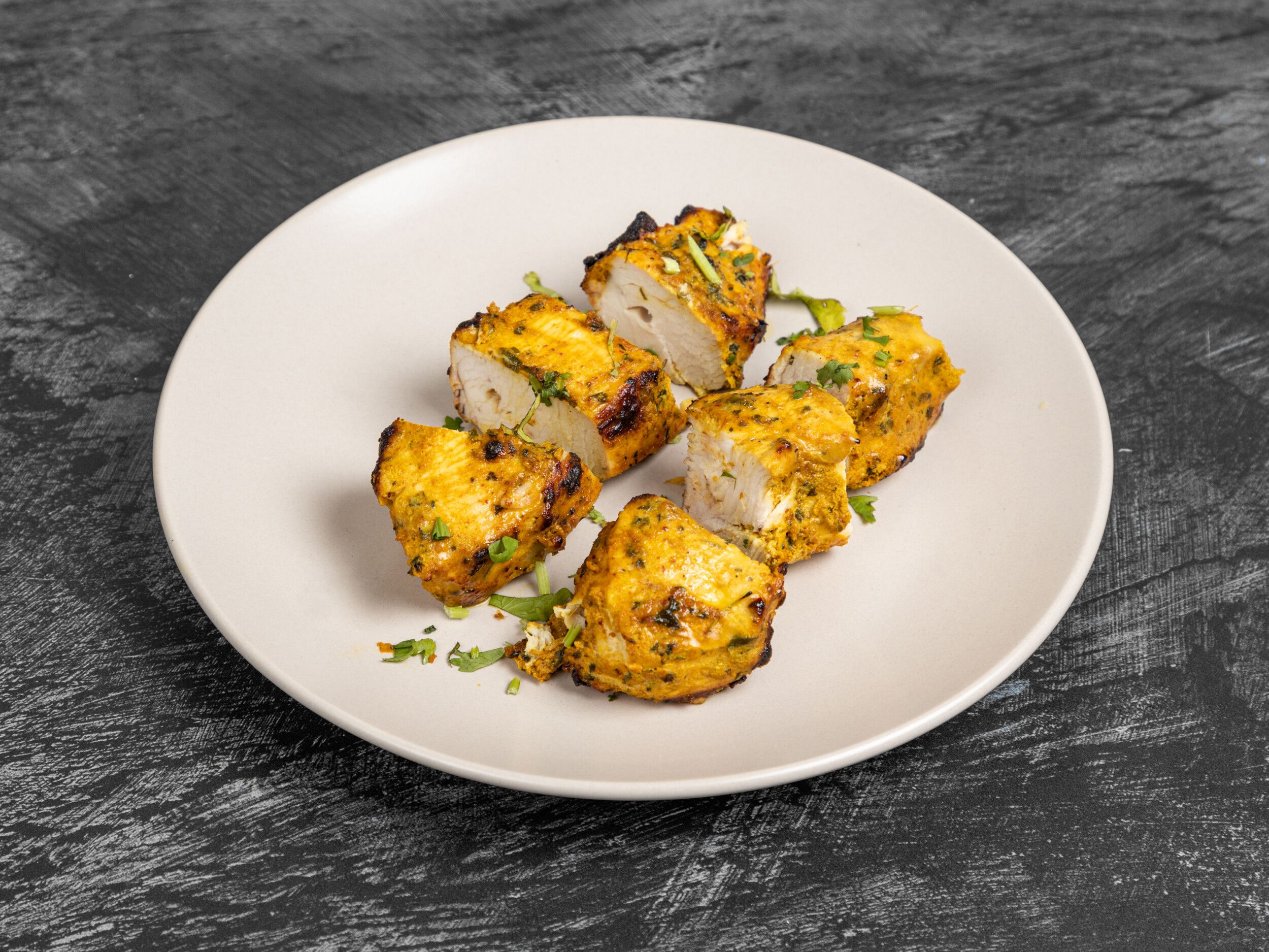Six pieces of tandoori paneer tikka, garnished with fresh herbs, on a white plate.