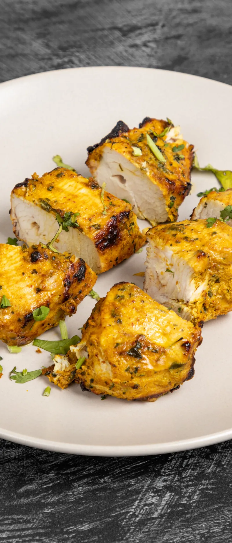 Six pieces of tandoori paneer tikka, garnished with fresh herbs, on a white plate.