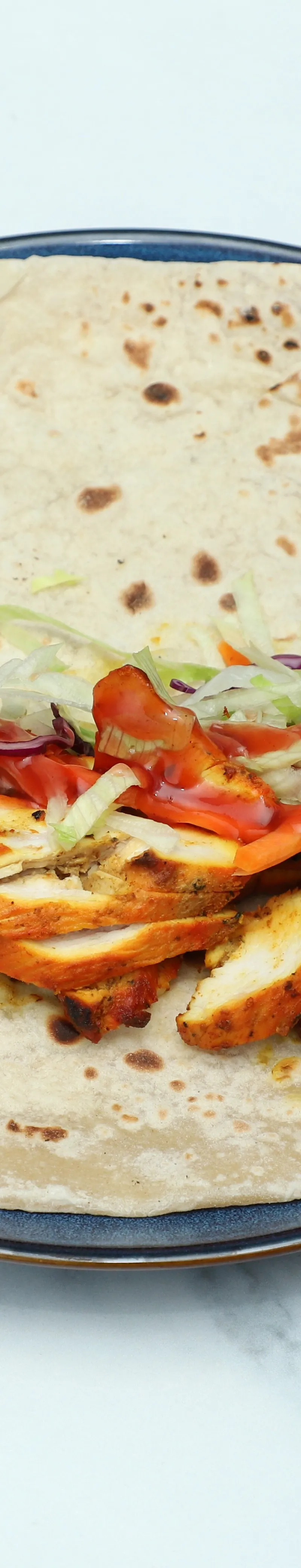 Chicken tikka pieces, shredded lettuce, and red sauce on a flatbread on a dark blue plate
