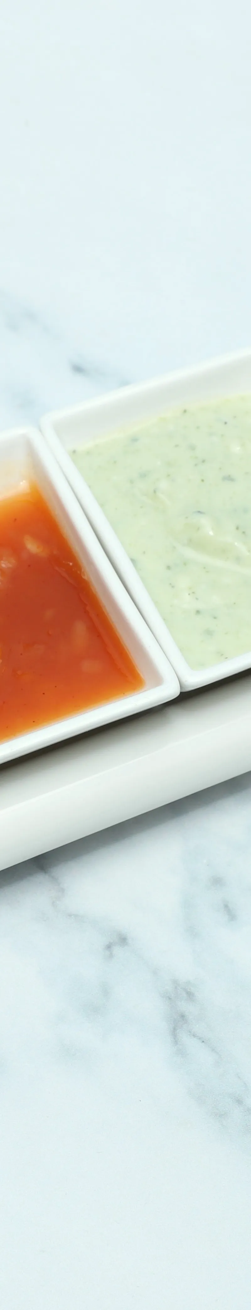 A white rectangular tray holds four small white containers with various condiments on a marble surface.
