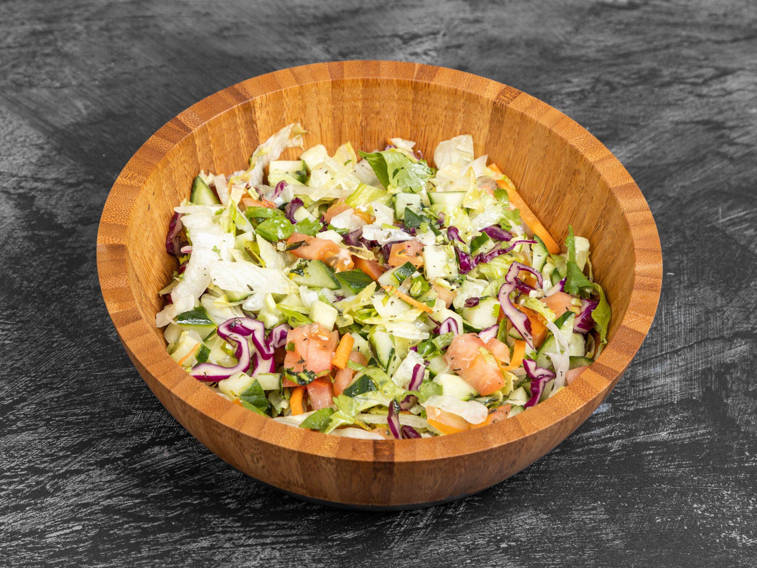 A vibrant mixed green salad in a wooden bowl with lettuce, cucumber, tomatoes, and red cabbage.
