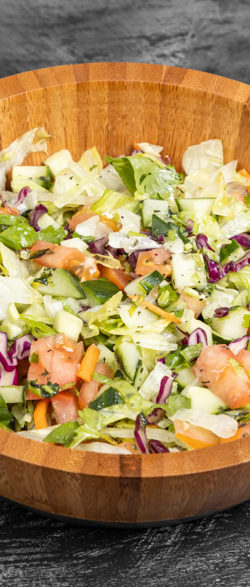A vibrant mixed green salad in a wooden bowl with lettuce, cucumber, tomatoes, and red cabbage.