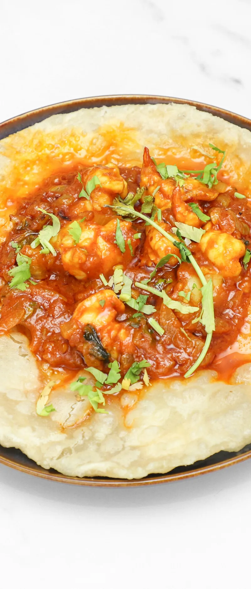 Top-down view of a golden fried puri topped with saucy prawn curry and fresh coriander.