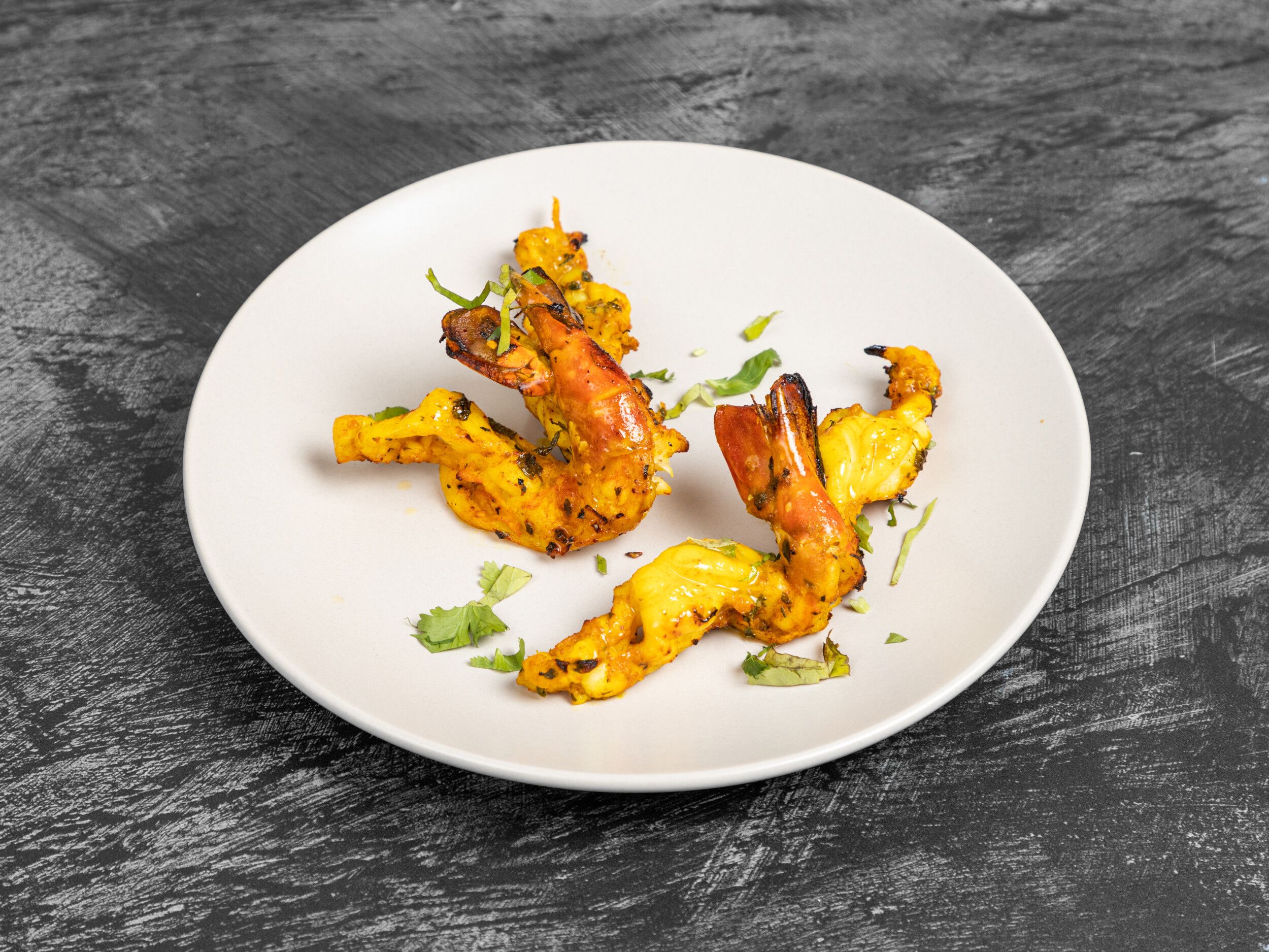 Grilled prawns on skewers, garnished with green herbs, served on a round white plate.