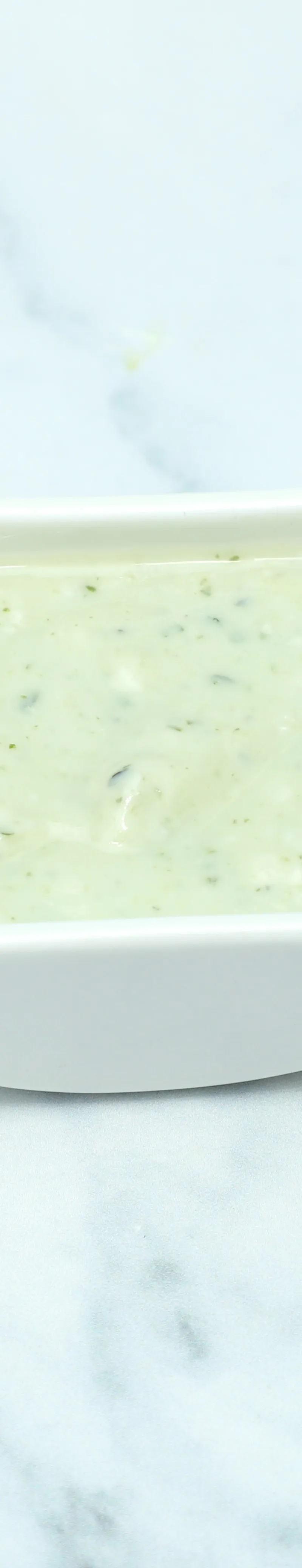 Small white square bowl filled with light green mint sauce sits on a marble surface.