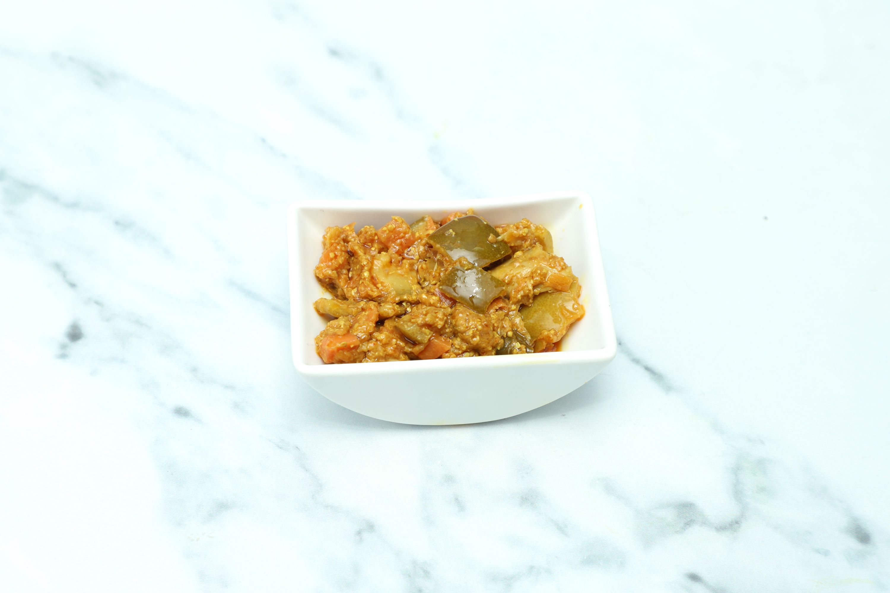 Small square white bowl filled with mixed vegetable pickle, including green and orange pieces