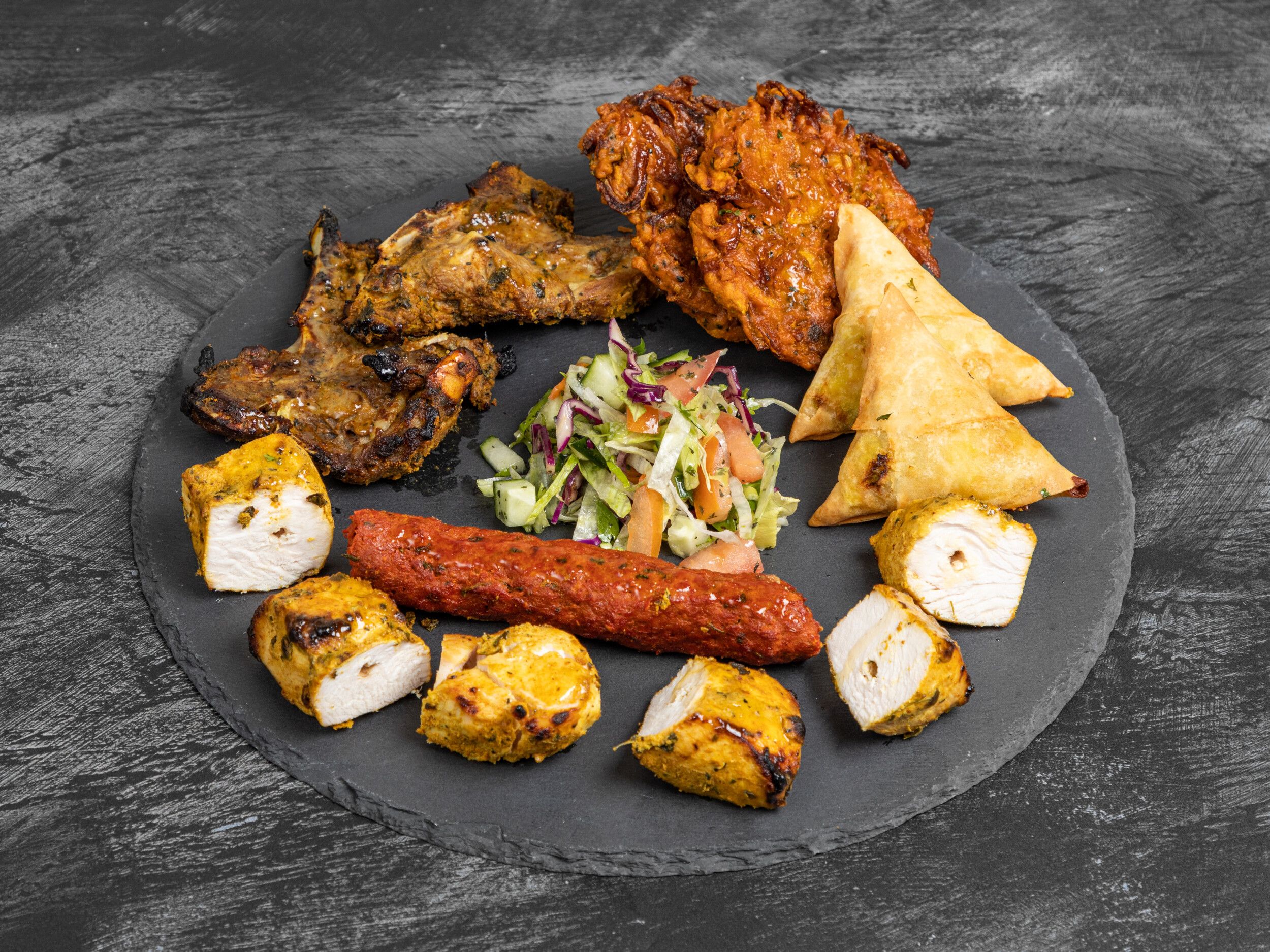 Mixed platter with lamb chops, onion bhajis, vegetable samosas, seekh kebab, chicken tikka, and salad