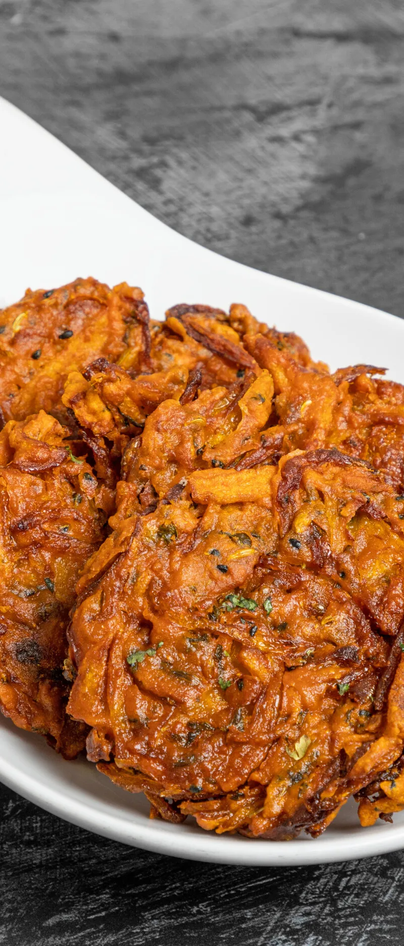 Several golden brown onion bhajis with green herbs in a white serving dish with a lemon wedge