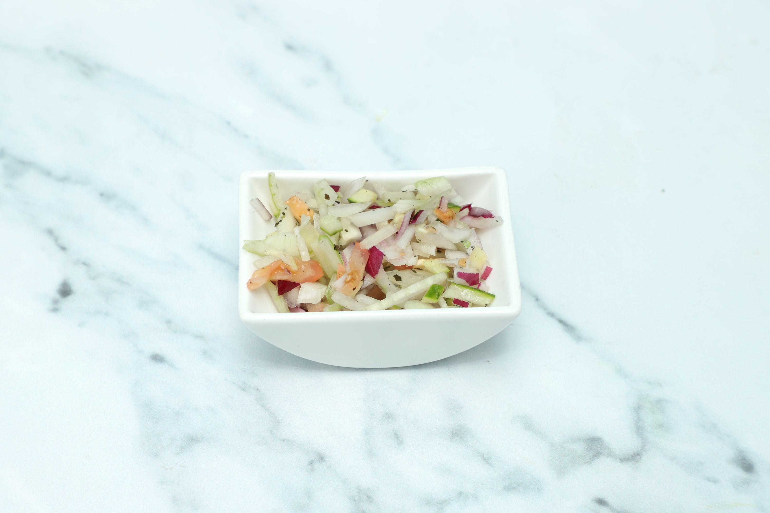 A small white bowl filled with diced red onion, white onion, cucumber, and orange red pepper.