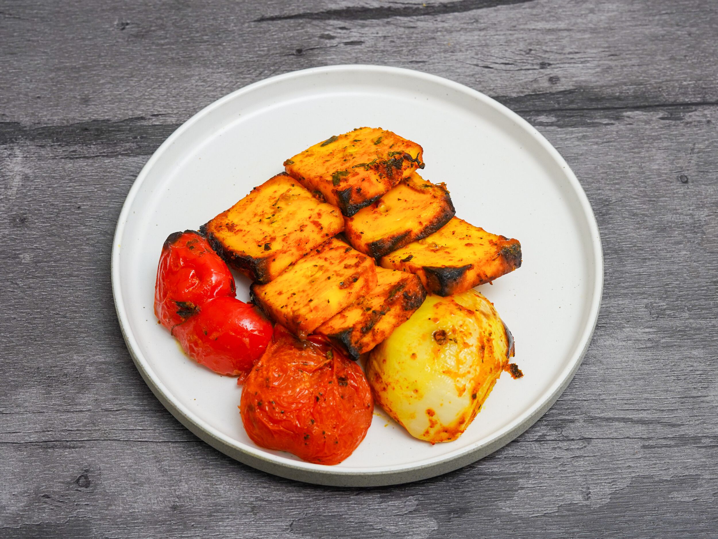 Grilled paneer tikka pieces arranged on a white plate with roasted red peppers and onions.