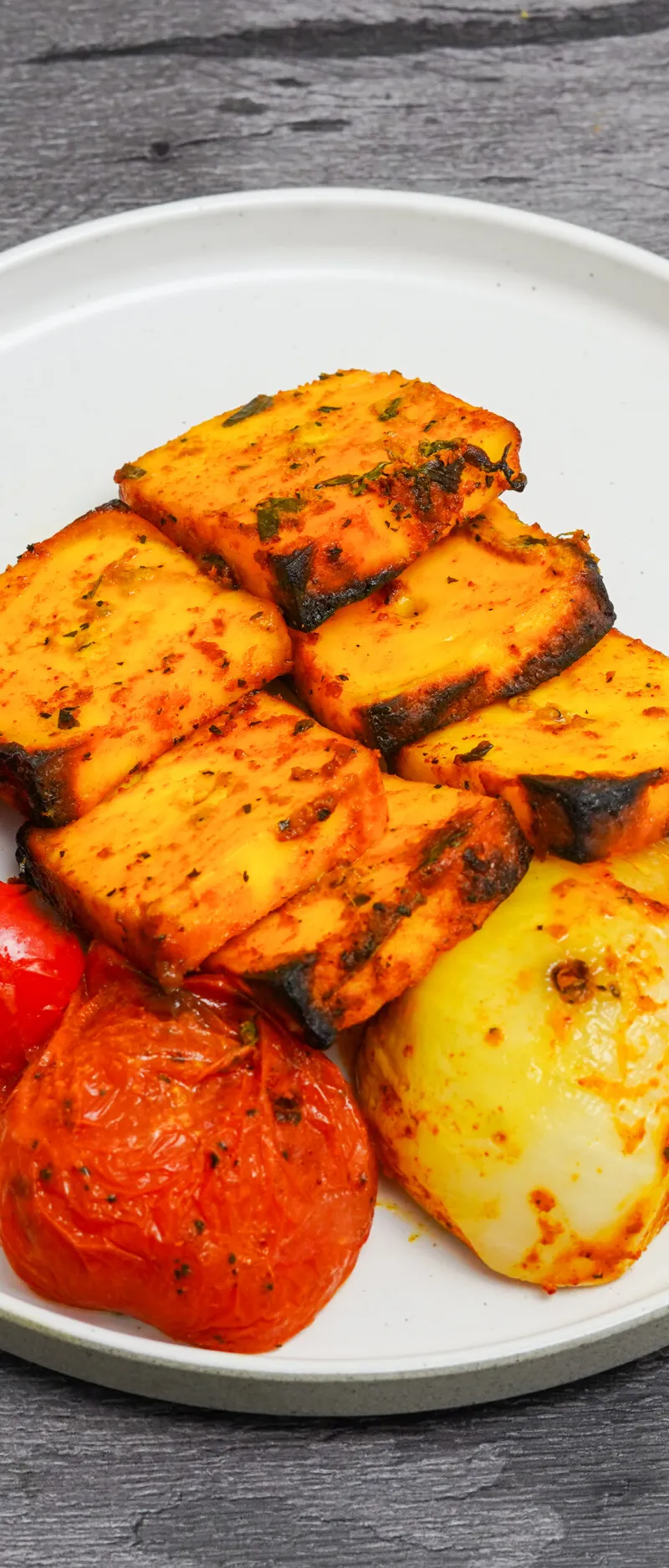 Grilled paneer tikka pieces arranged on a white plate with roasted red peppers and onions.