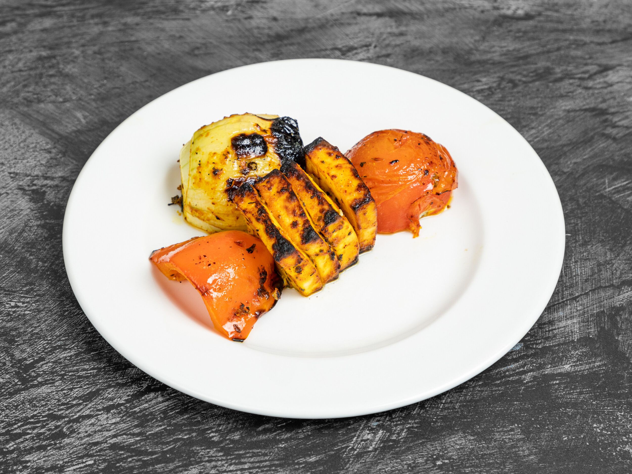 Grilled paneer slices, onion, red bell pepper, and tomato on a white plate