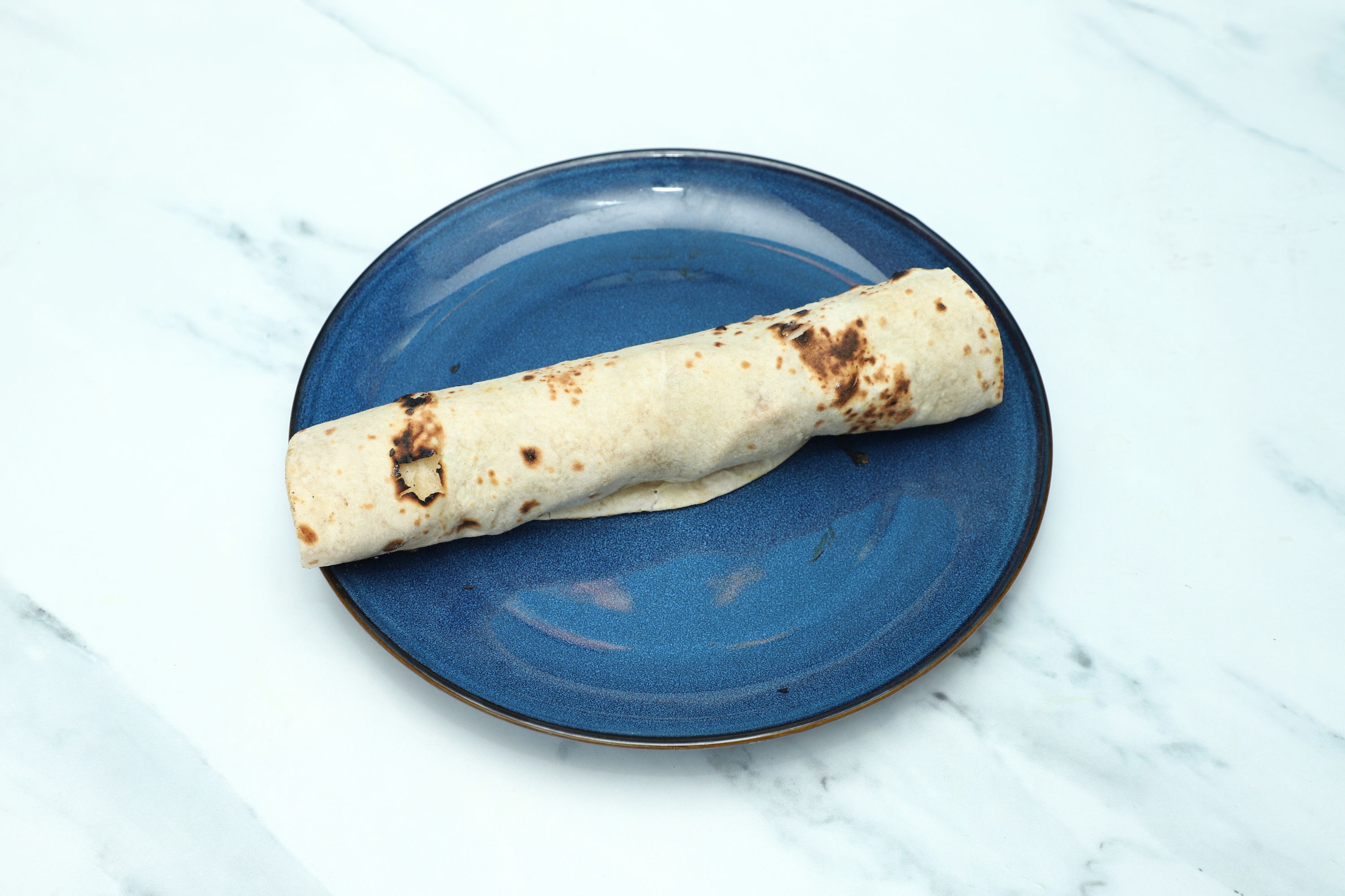 Single chapati bread, lightly charred from cooking, served on a round blue plate.