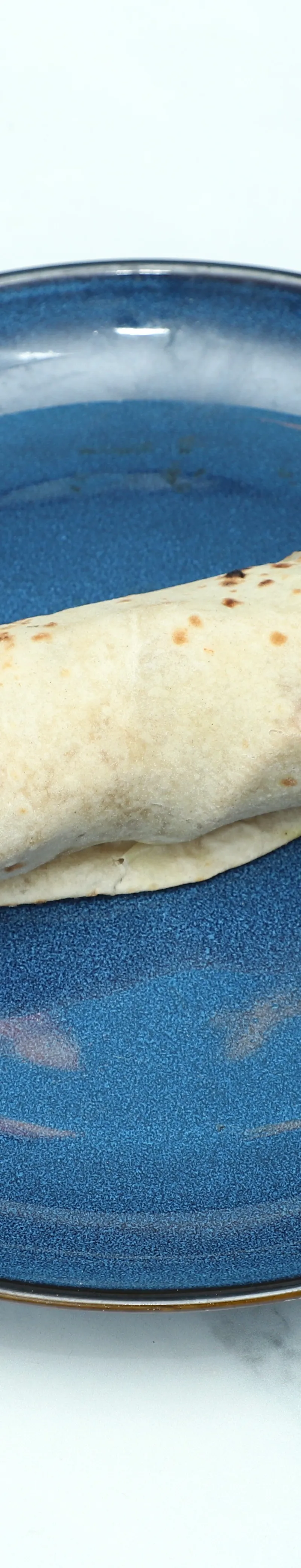 Single chapati bread, lightly charred from cooking, served on a round blue plate.