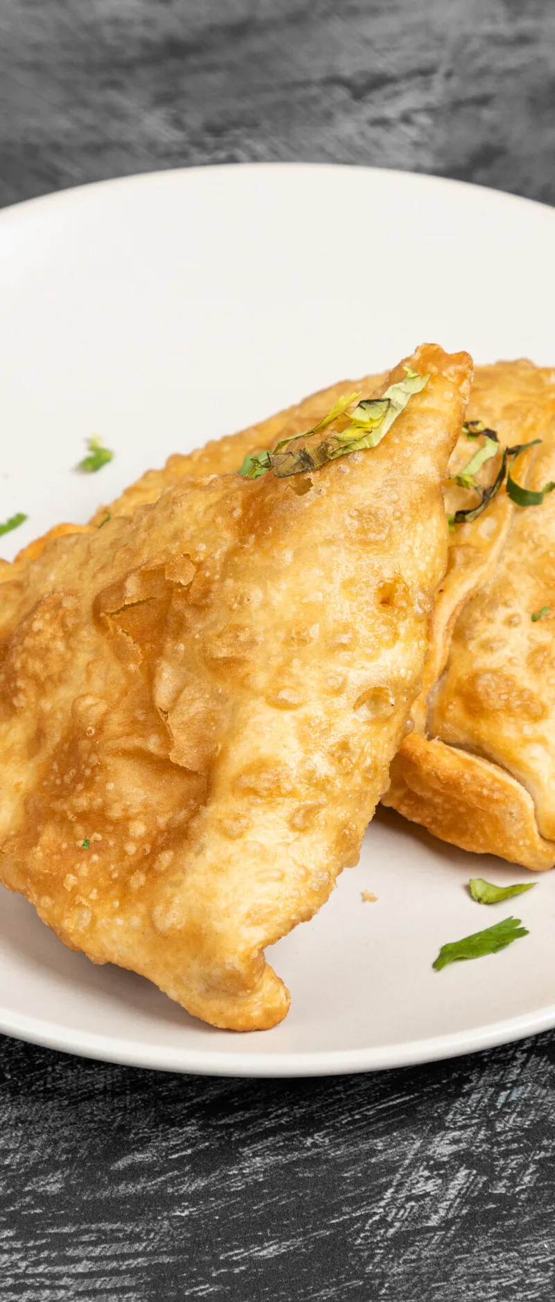 Two golden-brown fried large vegetable samosas adorned with fresh green herbs on a white plate.