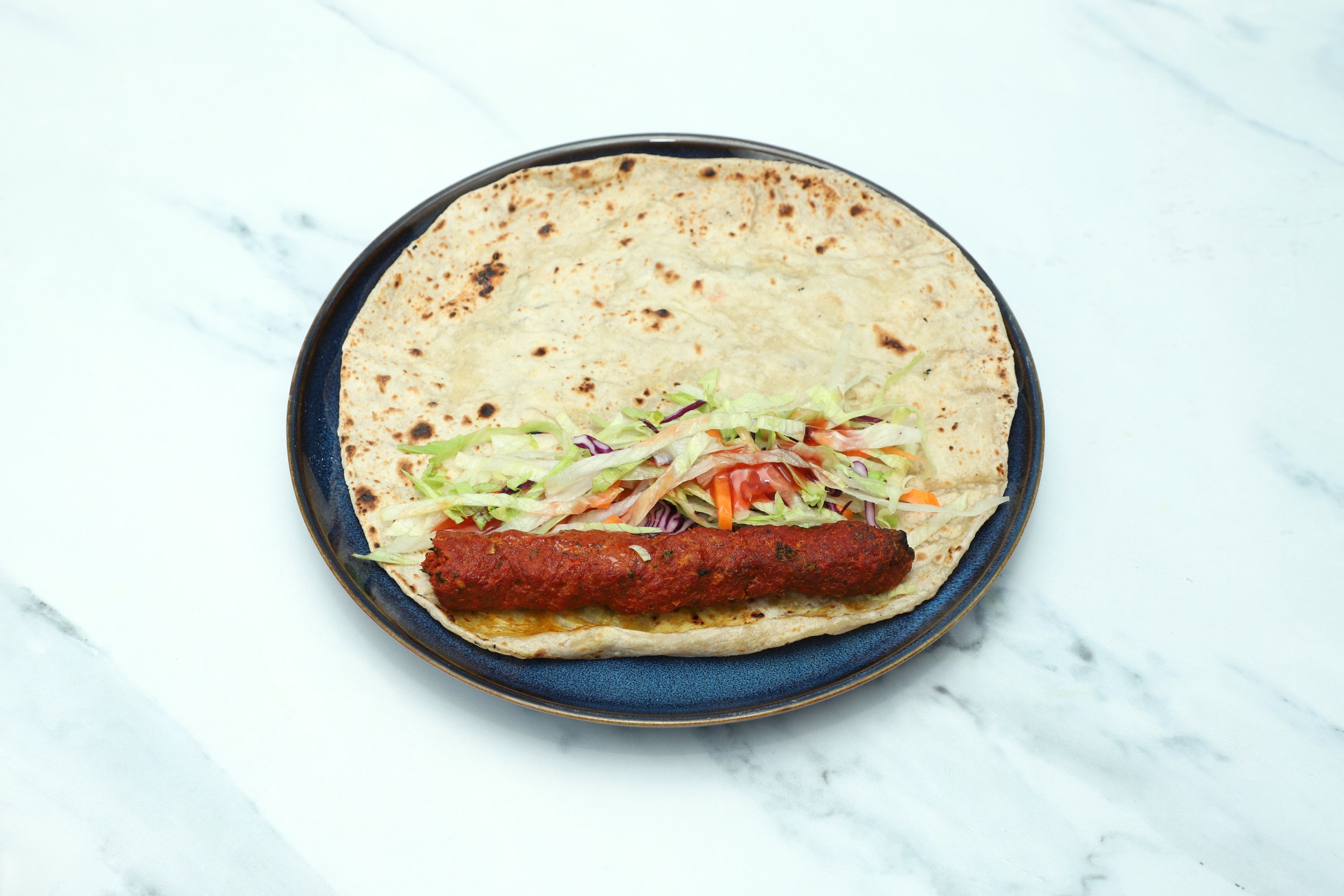A seekh kebab roll with a red kebab, shredded lettuce, and red cabbage on a blue plate.