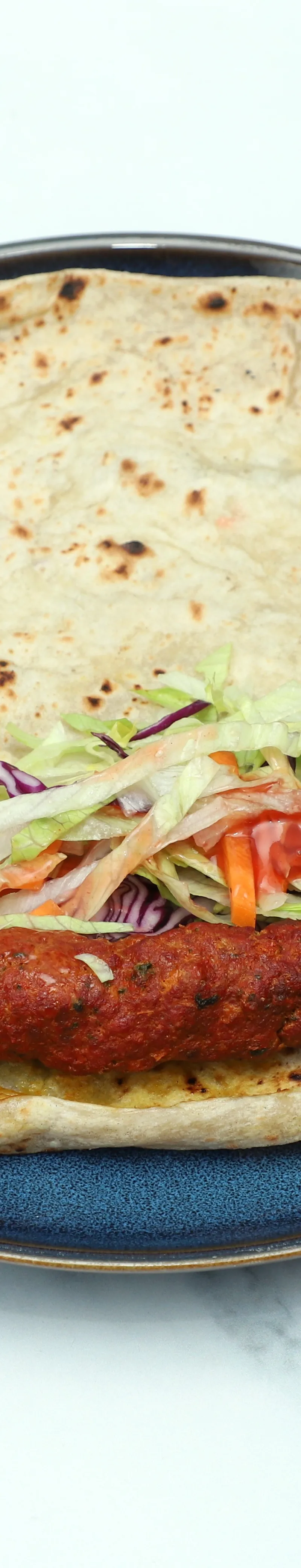 A seekh kebab roll with a red kebab, shredded lettuce, and red cabbage on a blue plate.