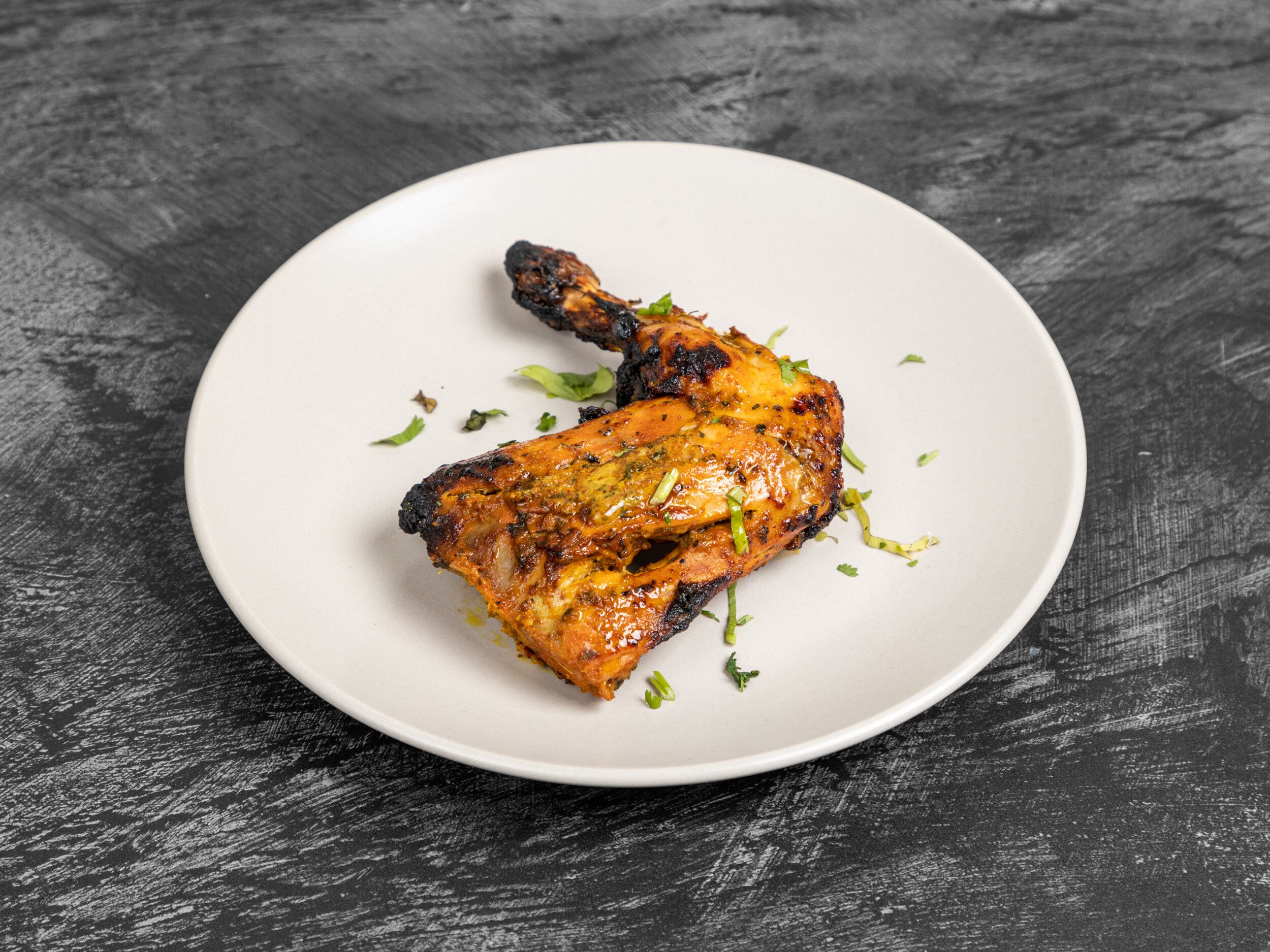 A single grilled tandoori chicken leg with charred marks and fresh herbs on a white plate.