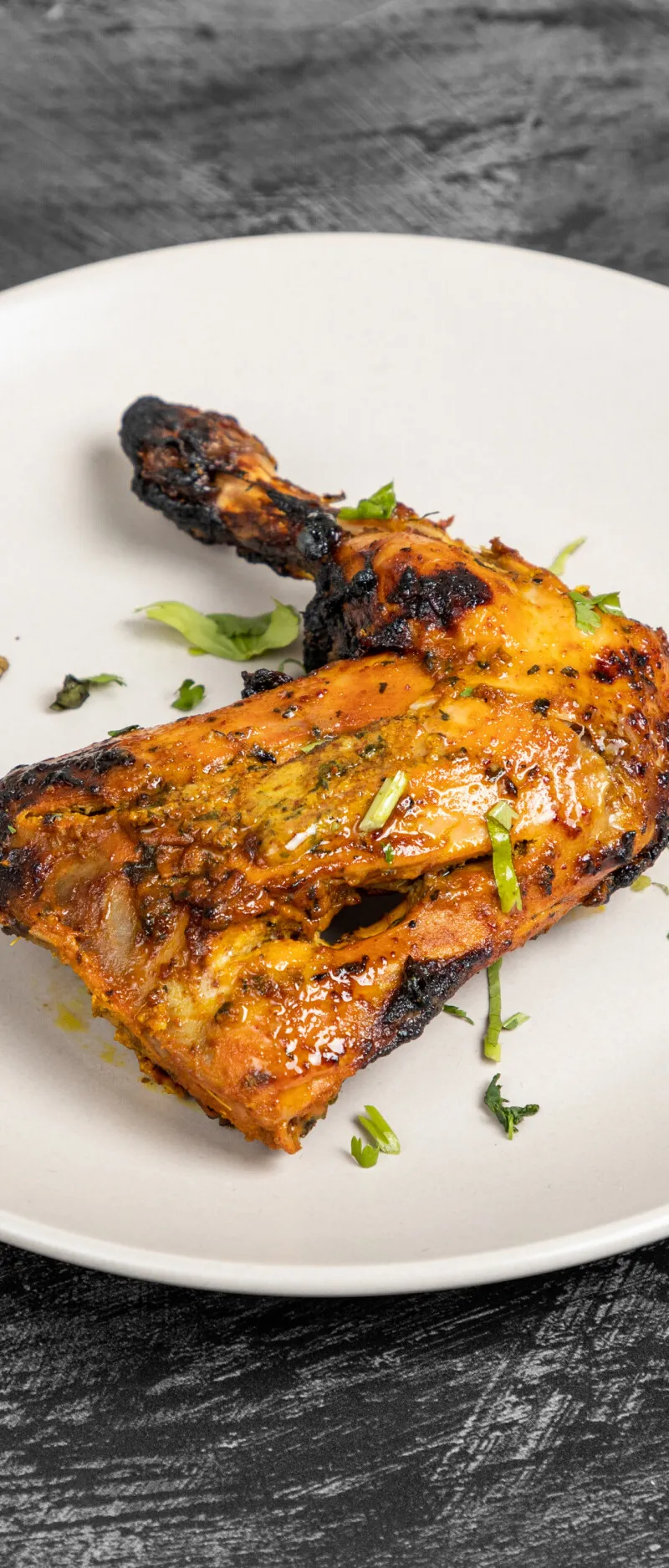 A single grilled tandoori chicken leg with charred marks and fresh herbs on a white plate.