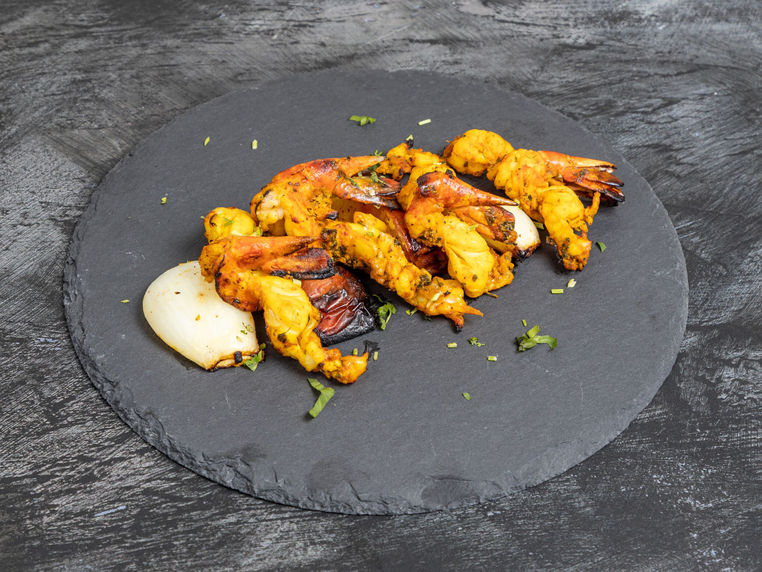 Grilled shrimp tikka and charred onion and peppers on a dark grey slate serving platter.