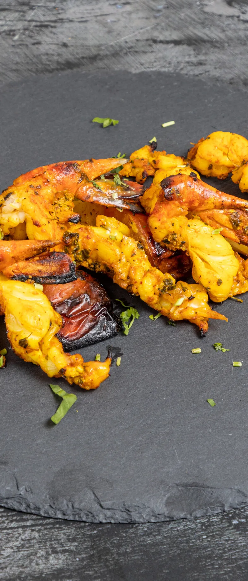 Grilled shrimp tikka and charred onion and peppers on a dark grey slate serving platter.