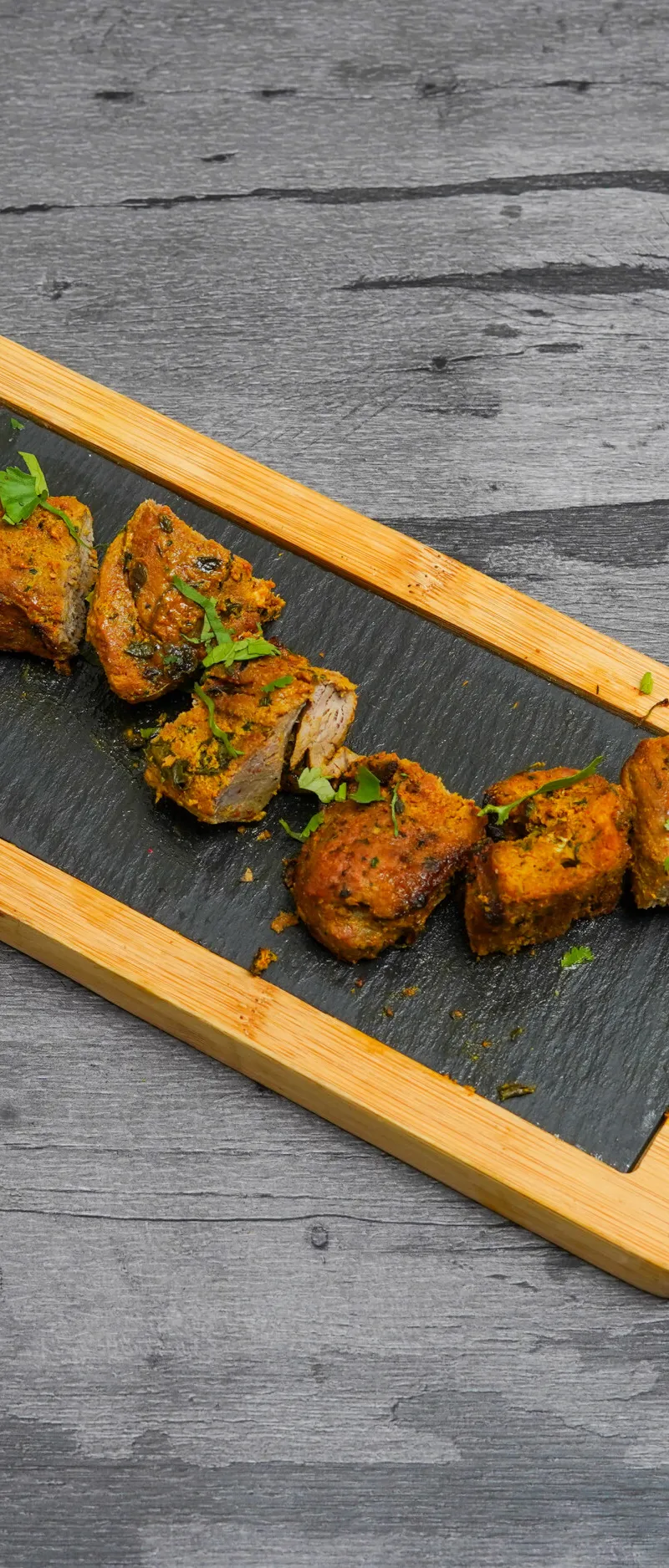 Lamb tikka pieces and sliced white onions on a black slate serving board with wooden trim and handle.