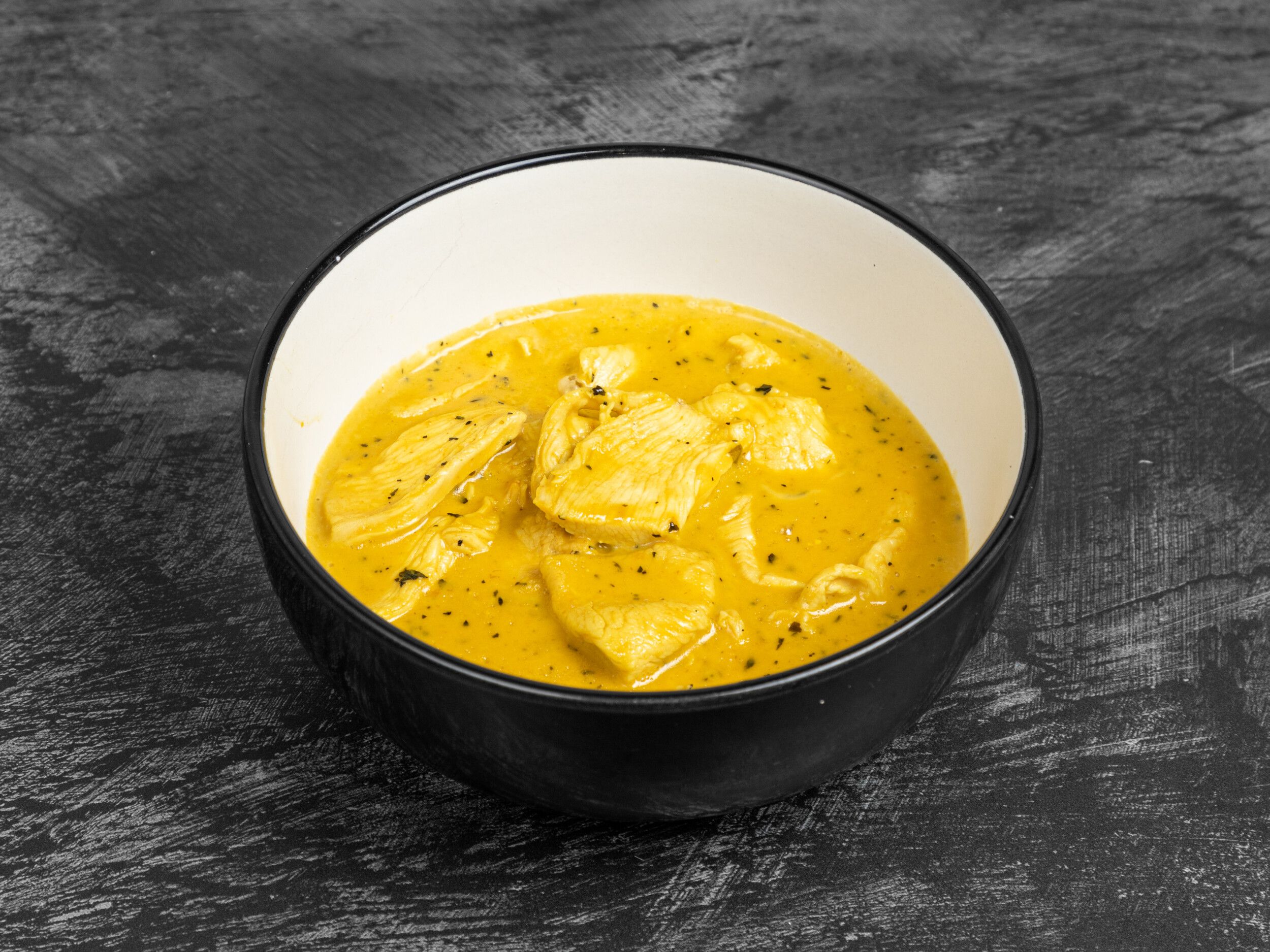 Chicken pieces in a rich yellow curry sauce, garnished with herbs, in a black and white bowl.