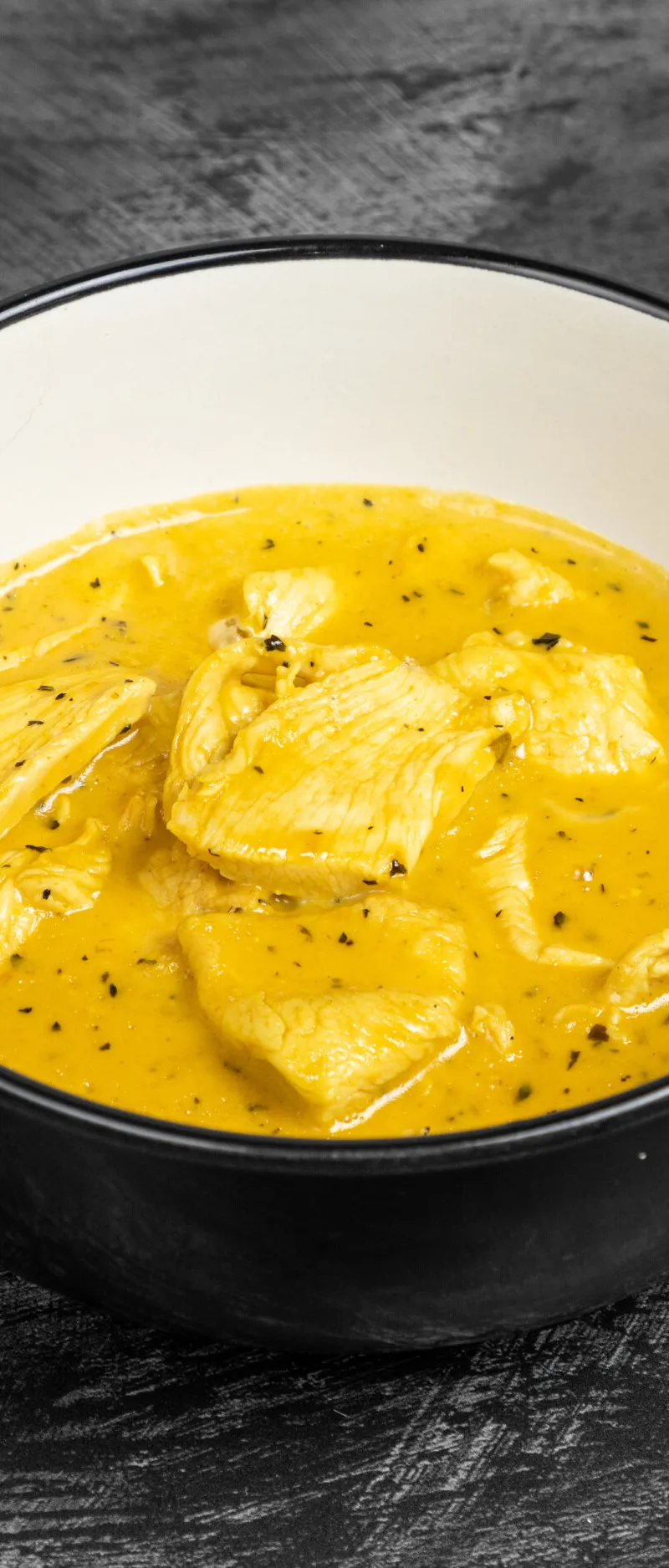 Chicken pieces in a rich yellow curry sauce, garnished with herbs, in a black and white bowl.