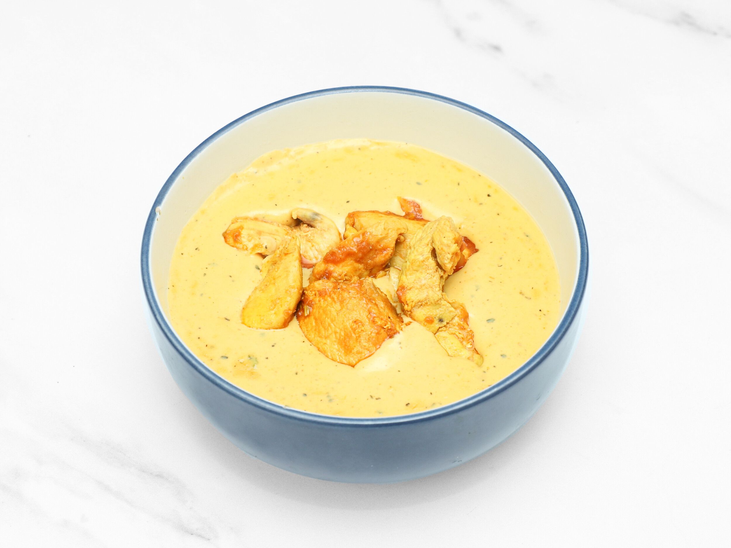 Tender pieces of chicken in a rich, creamy yellow curry, served in a blue bowl