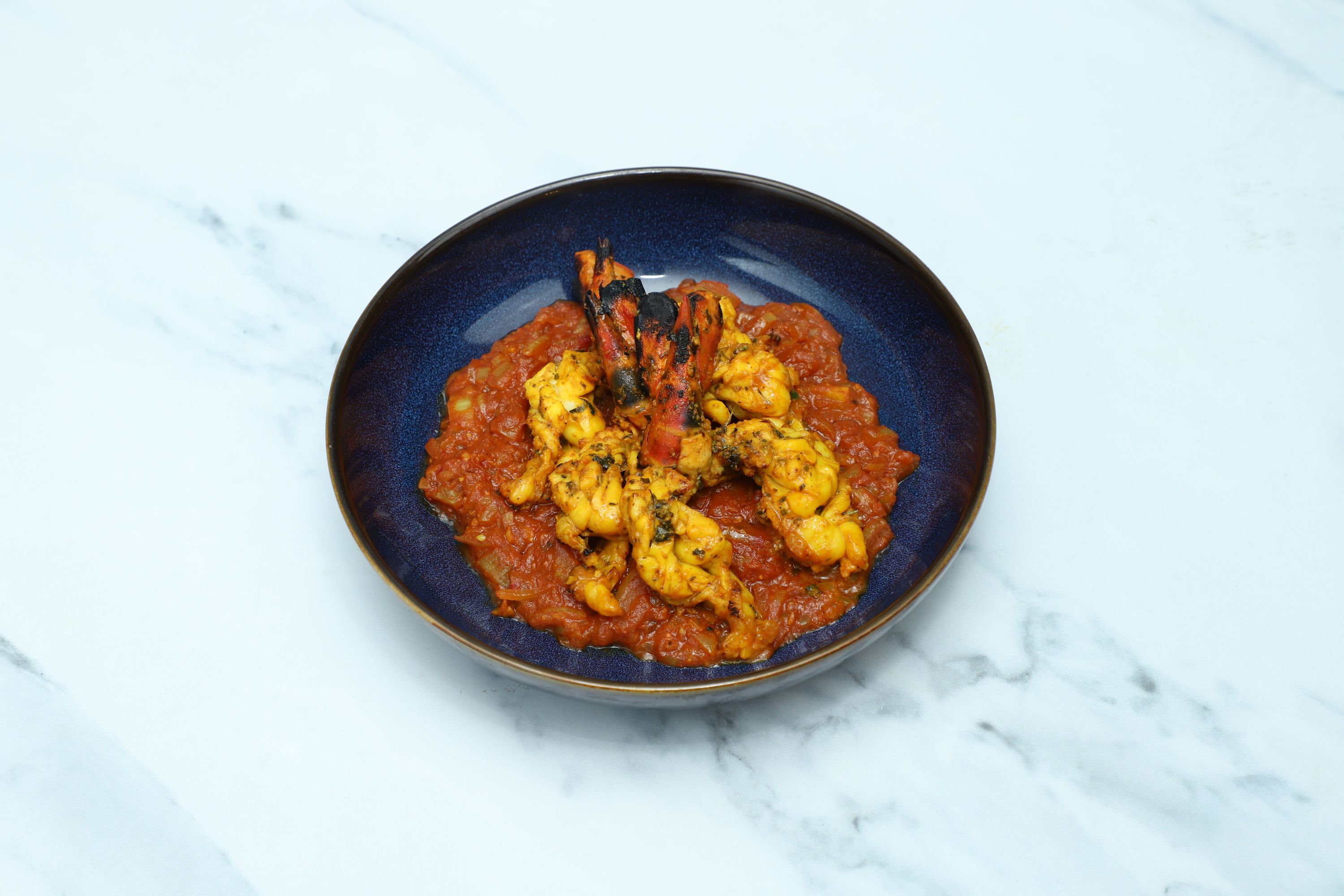 Tandoori king prawns with charred tails, served on a bed of vibrant tomato and onion masala.