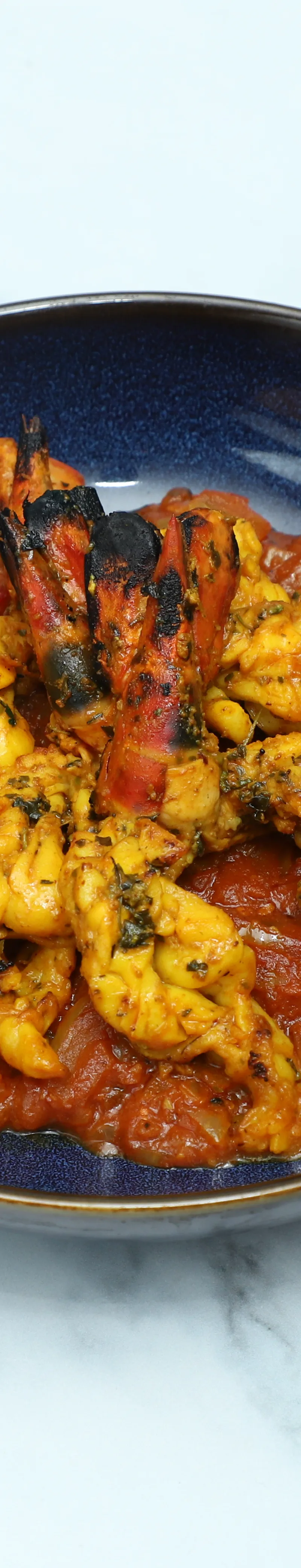 Tandoori king prawns with charred tails, served on a bed of vibrant tomato and onion masala.