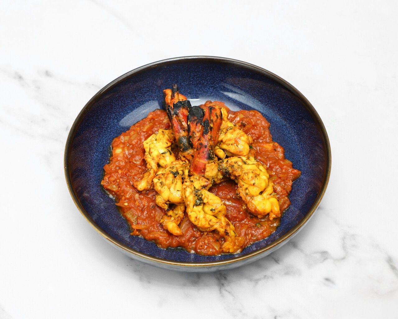 Grilled jumbo prawns and smaller prawns on a bed of sauteed tomatoes and onion sauce.