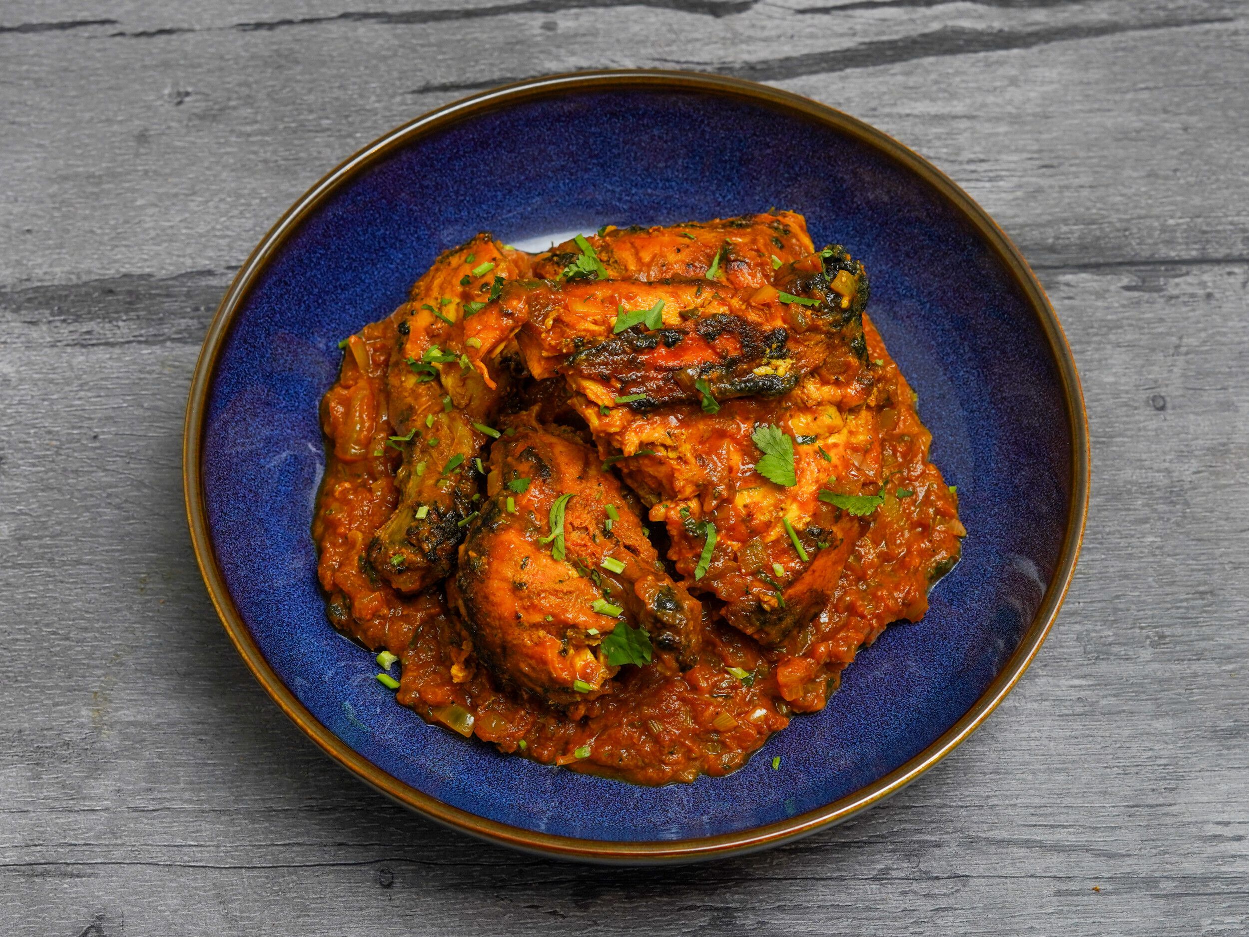 A vibrant chicken curry garnished with fresh green coriander, served in a deep blue bowl.