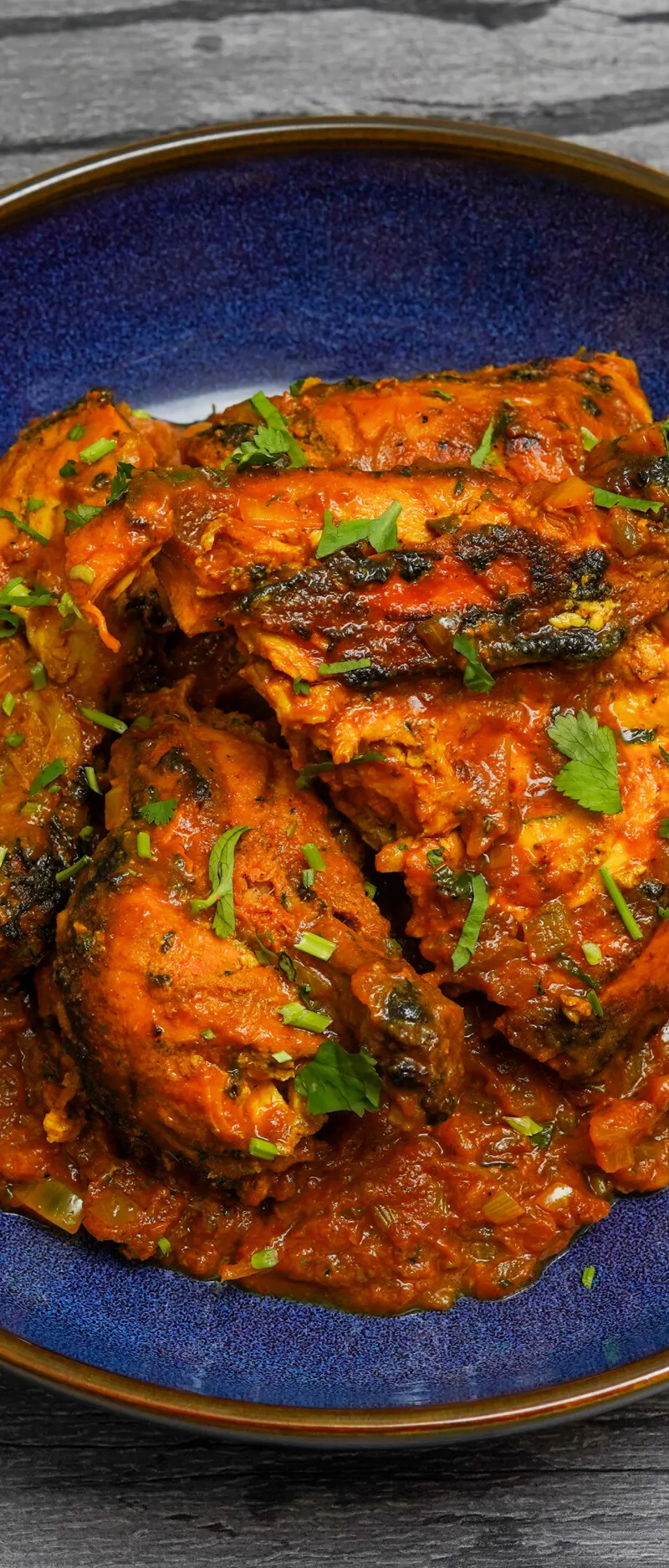 A vibrant chicken curry garnished with fresh green coriander, served in a deep blue bowl.